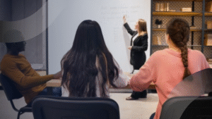 Guru menjelaskan materi di depan kelas dengan siswa yang fokus belajar, mencerminkan program Sekolah Siap menghadapi tantangan global.