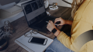 Seorang wanita bekerja di laptop dengan tampilan desain web, mencatat ide di buku, merepresentasikan layanan profesional jasa website development.