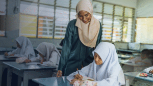 Guru mendampingi siswi menulis di kelas sebagai wujud inovasi belajar yang mendorong kreativitas dan pemahaman lebih mendalam