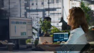 Seorang profesional wanita sedang menganalisis data pemasaran di komputer di kantor modern, menggambarkan solusi cerdas pemasaran bisnis berbasis data dan teknologi.