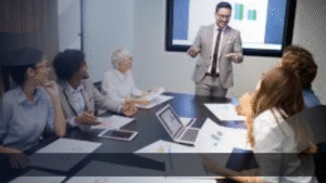 Tim profesional sedang berdiskusi di ruang rapat dengan grafik pemasaran ditampilkan di layar, mewakili kolaborasi dalam menyusun strategi marketing kit digital untuk pertumbuhan bisnis.