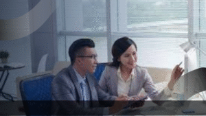 Dua profesional sedang berdiskusi di depan komputer dalam suasana kerja modern, menggambarkan kolaborasi dan manajemen strategis dalam pengembangan Sekolah Internasional yang berstandar global.