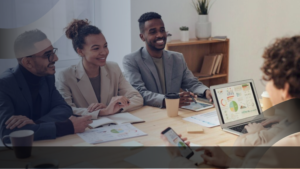 Tim profesional berdiskusi dalam rapat sambil meninjau dashboard data di laptop, merepresentasikan strategi konsultan pendidikan dalam optimalisasi platform pembelajaran digital.