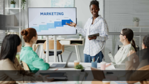 Tim digital marketing meninjau tahapan strategi campaign di layar presentasi, menggambarkan potensi distorsi pesan produk dalam proses komunikasi pemasaran.