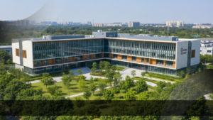 Pemandangan udara (aerial view) sebuah gedung sekolah internasional modern yang dikelilingi taman hijau dan pepohonan rimbun, dengan teks judul "Bagaimana Prosedur Membangun Sekolah Internasional bersama Konsultan Pendidikan".